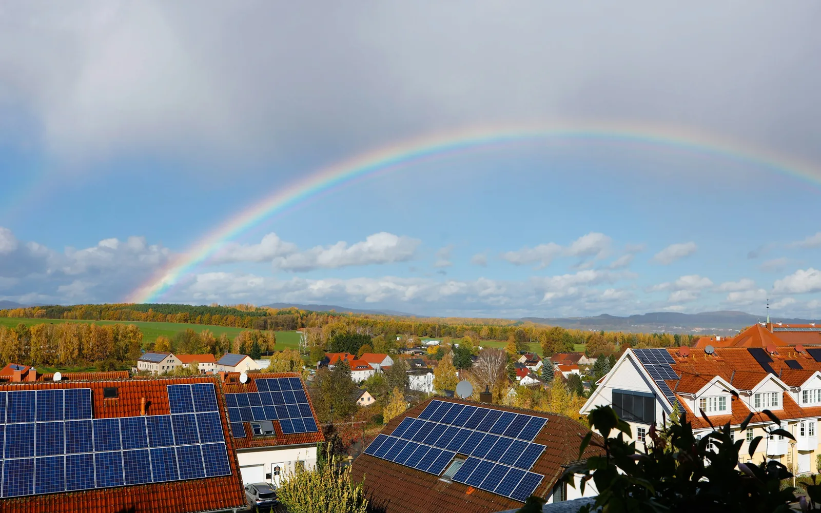 Regenbogen über einem Wohngebiet mit Solarmodulen auf mehreren roten Ziegeldächern im Herbst (Oberscheinfeld, Landkreis Neustadt an der Aisch-Bad Windsheim)