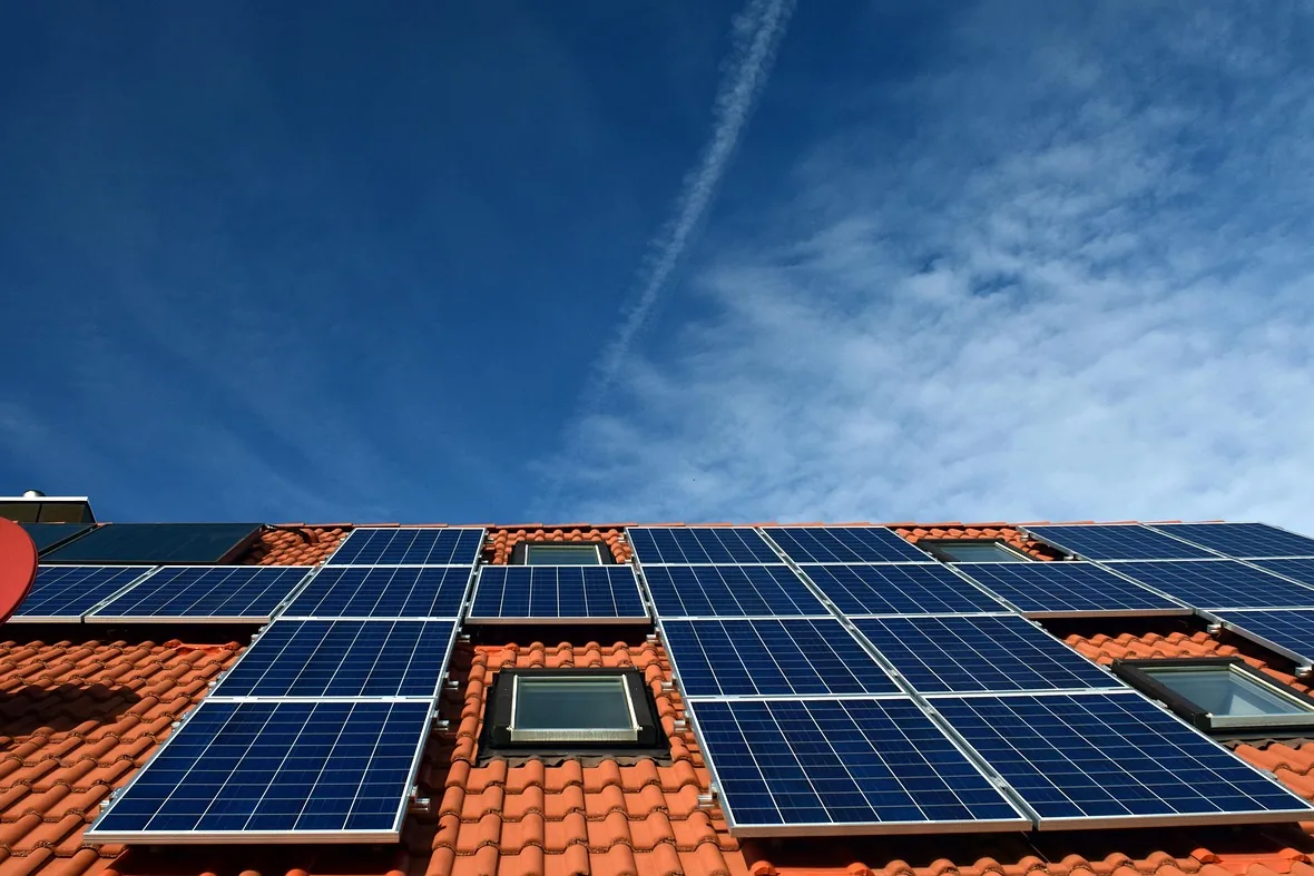 Blaue Solarmodule zwischen Dachfenstern auf einem orangeroten Ziegeldach unter leicht bewölktem Himmel (Kirchberg, Zwickau)