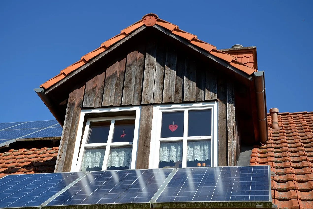 Holzverkleidete Dachgaube mit weißen Sprossenfenstern, davor Solarmodule auf einem roten Ziegeldach (Zeil, Landkreis Haßberge)