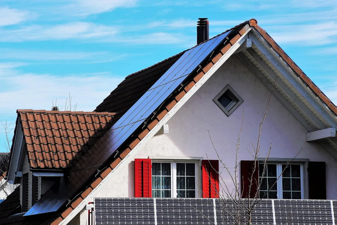 Weißes Giebelhaus mit roten Fensterläden, Solarmodulen auf dem Dach und am Balkongeländer