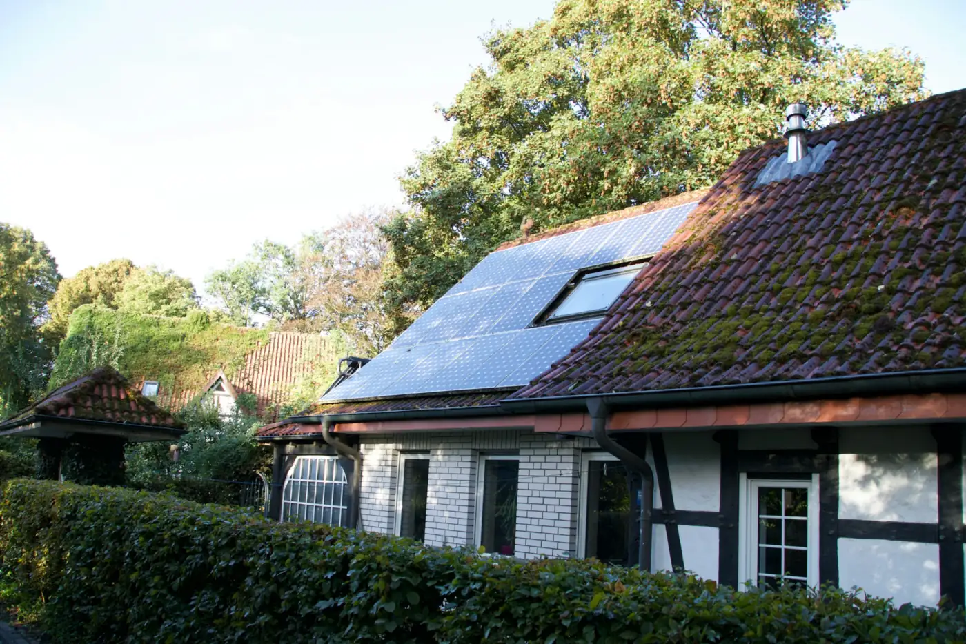 Fachwerkhaus mit Solarmodulen rund um ein Dachfenster, davor eine hohe Hecke (Prisdorf, Kreis Pinneberg)