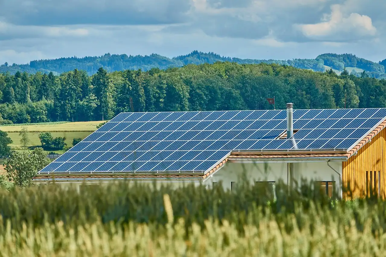 Großes Hausdach fast vollständig mit Solarmodulen belegt, dahinter bewaldete Hügel und Felder