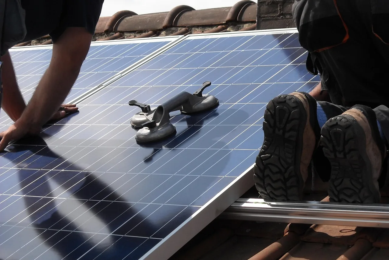 Zwei Monteure legen ein Solarmodul mit Saugheber auf die Montageschienen eines Ziegeldachs (Ober-Mörlen, Wetteraukreis)