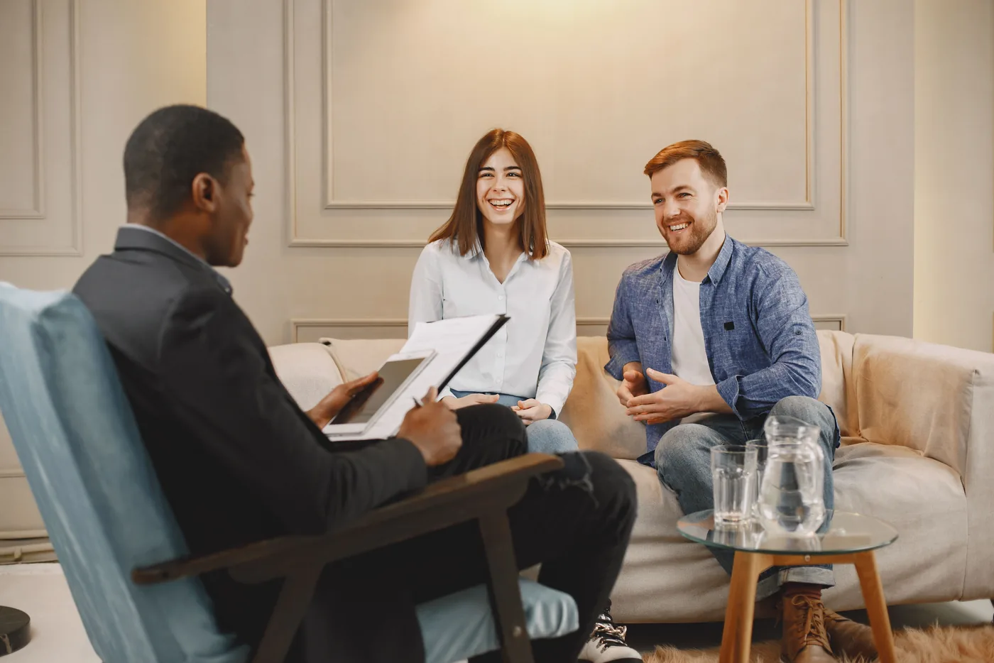 Berater mit Tablet bespricht im Wohnzimmer Unterlagen mit einem jungen Paar auf dem Sofa (Rickling, Kreis Segeberg)