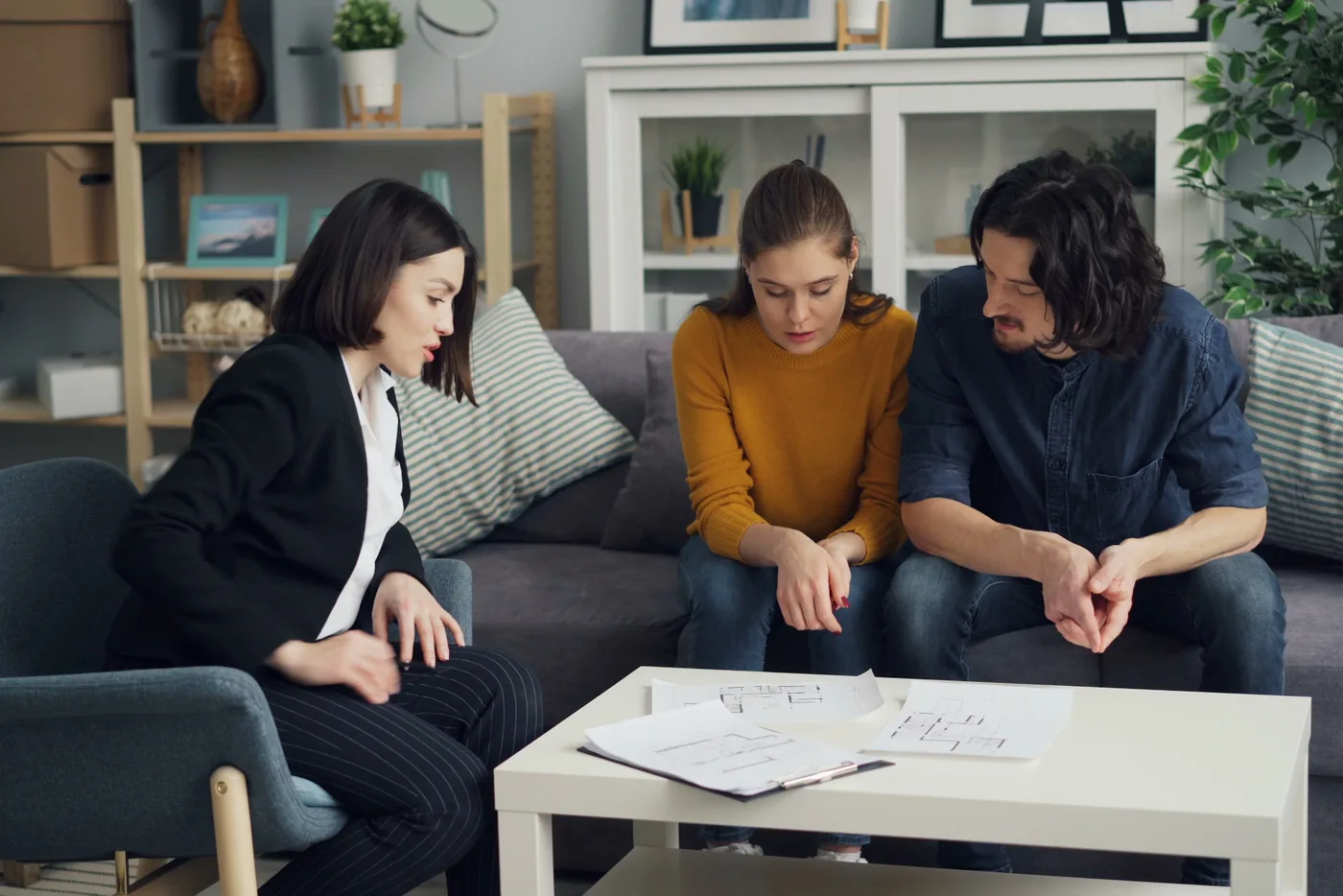 Beraterin erklärt einem Paar auf dem Sofa Unterlagen, die auf dem Couchtisch liegen (Daaden, Landkreis Altenkirchen)